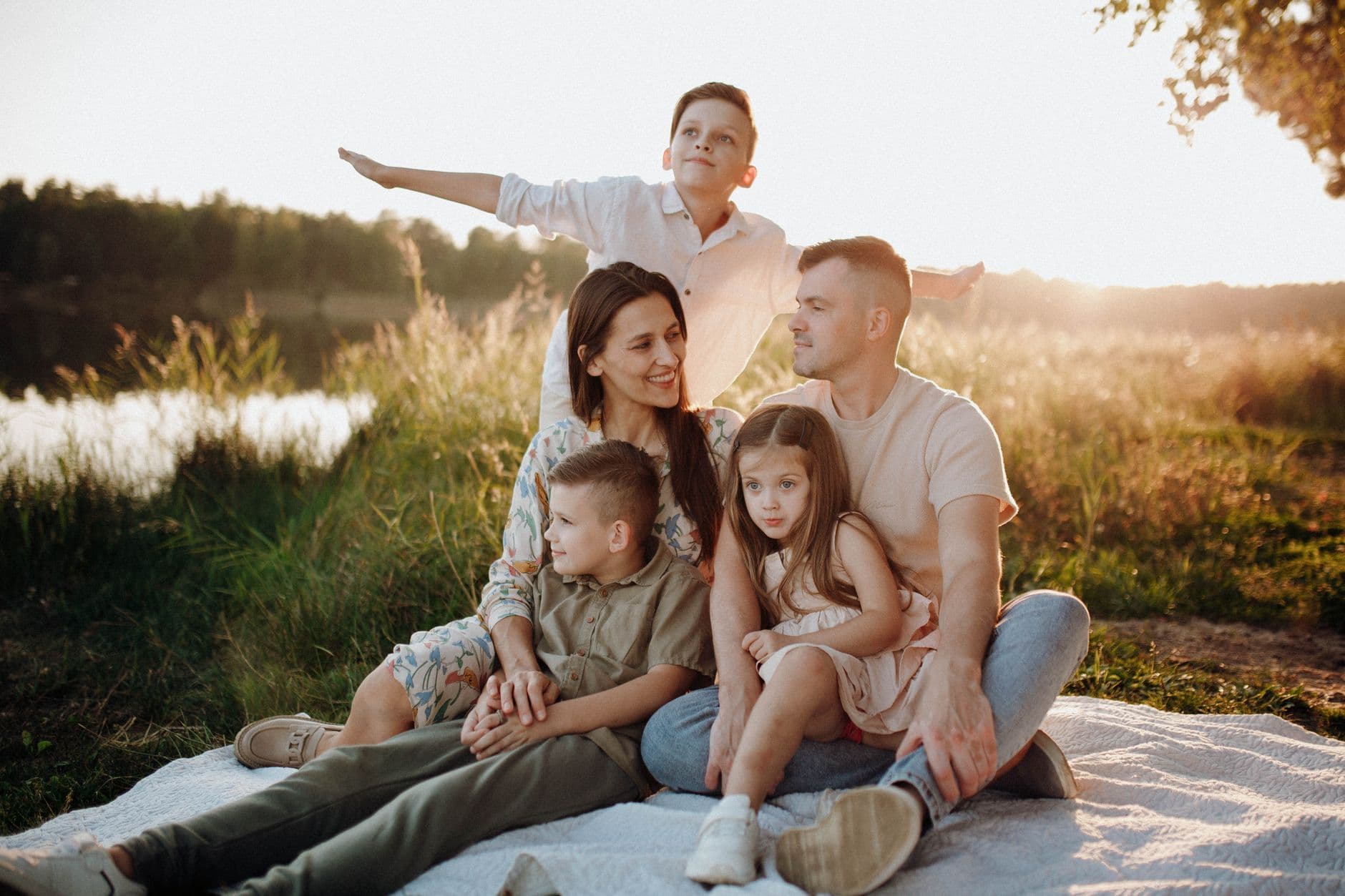 A family of five enjoying a serene picnic in a sunlit meadow during sunset.